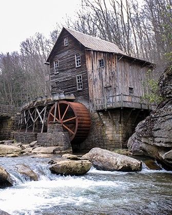 An old wood building with a water wheel stands next to a rushing river. 